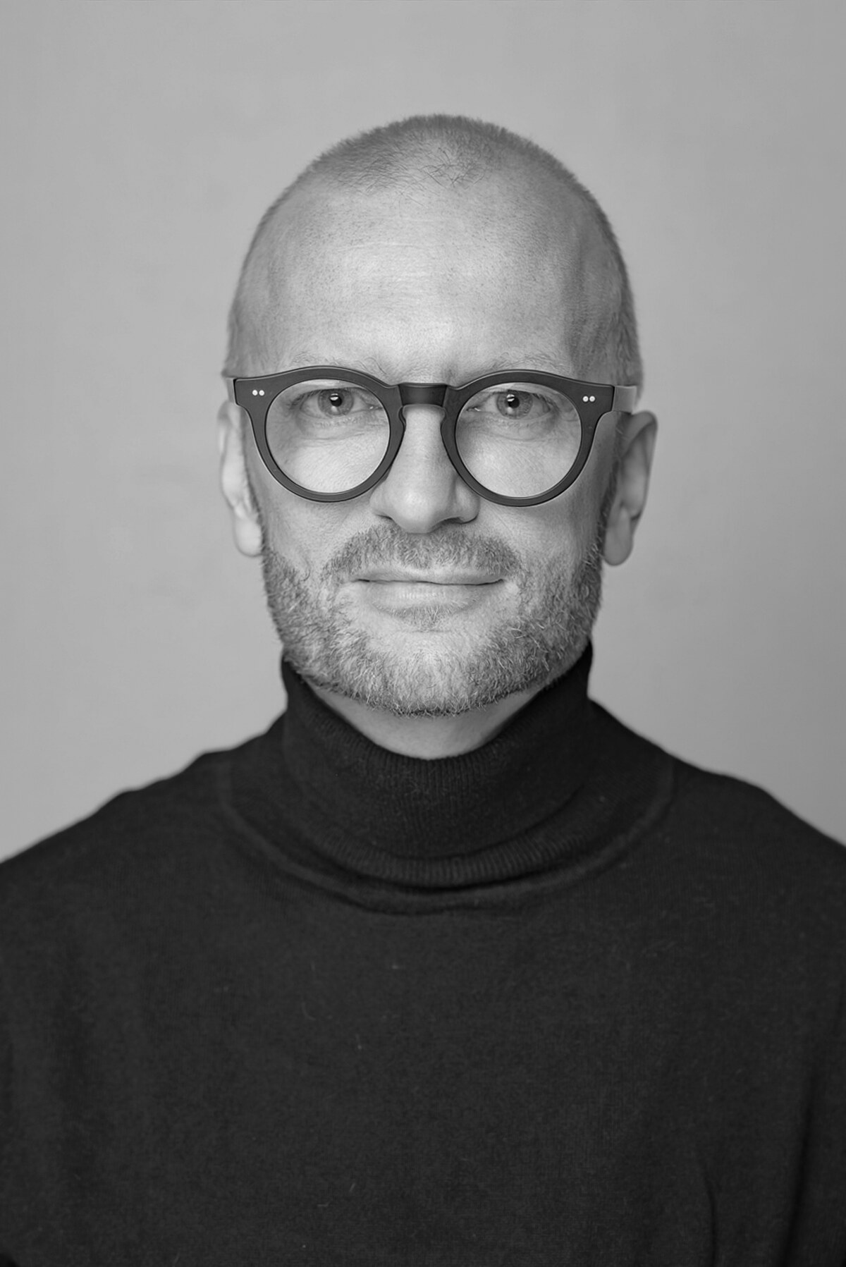 Mein Porträt: Ich blicke mit dunkler Brille und schwarzem Rollkragenpullover direkt in die Kamera.